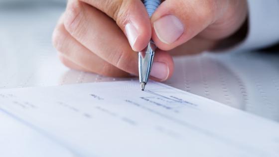 A Male Hand Filling Out The Amount On A Cheque